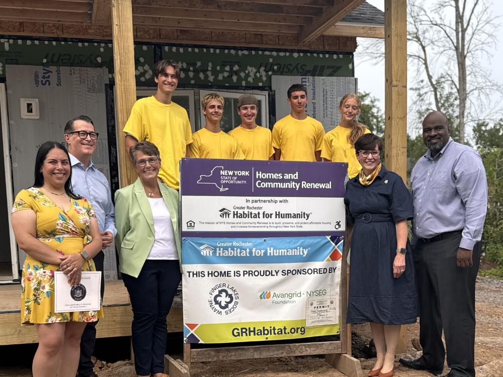 A group photo in front of a house under construction with Habitat for Humanity signs.